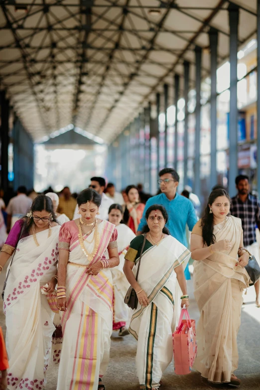 a group of women in white saris walk under the roof of an indoor building