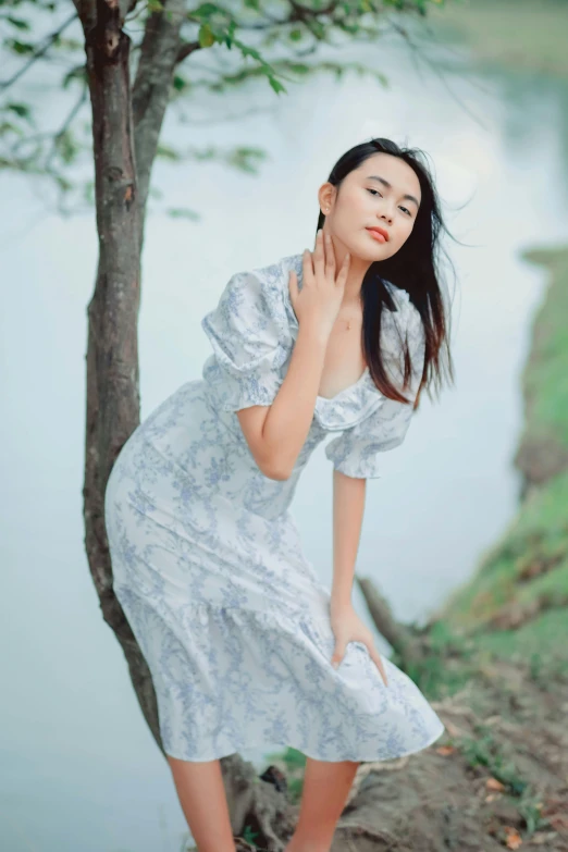 an asian woman in a floral dress standing beside a tree