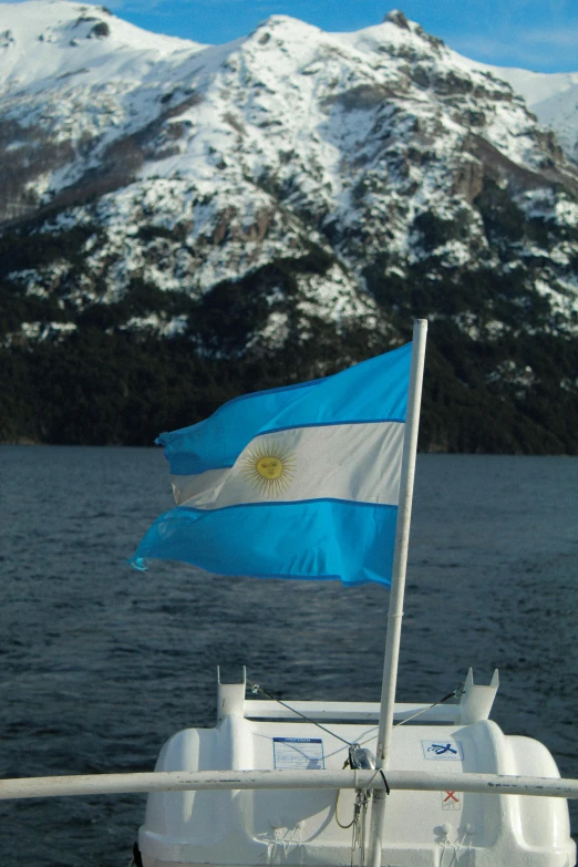 the flag on a boat on a large body of water with snow covered mountains behind it