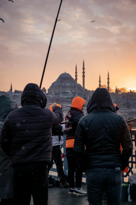 several people are standing on a bridge watching the sun go down