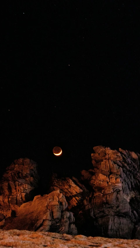 the moon is setting above some rocks and a hill
