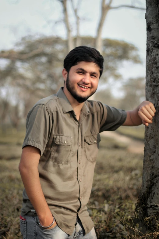 a young man smiles by a tree in the woods