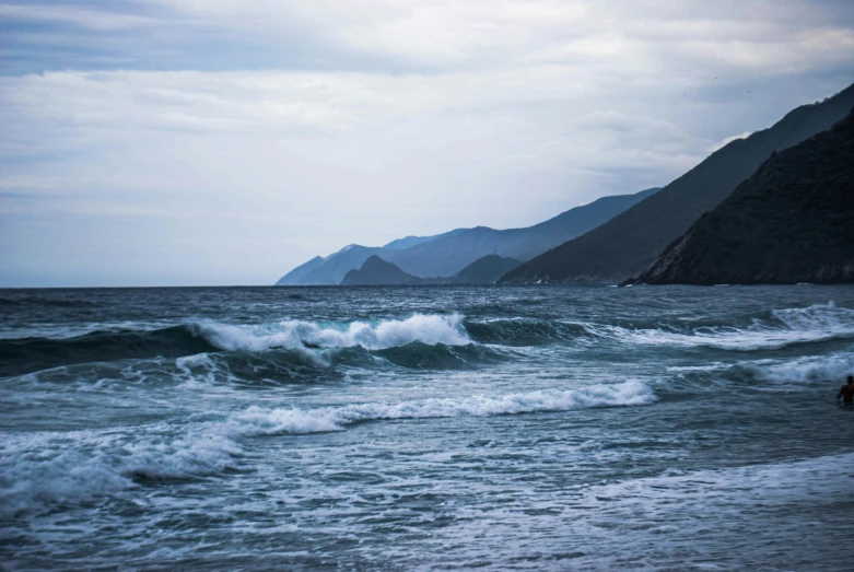 there are waves rolling into shore with a mountain in the background