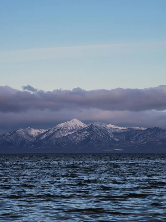 snow covered mountains rise over the ocean with blue water