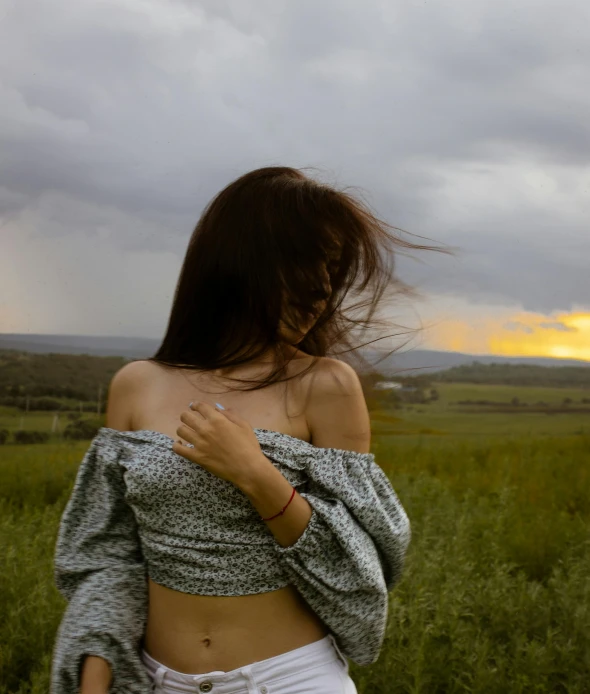 woman in a field with cloudy sky and light colored clouds