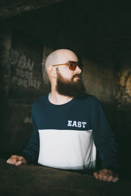 a bearded man wearing sunglasses standing next to a brick wall