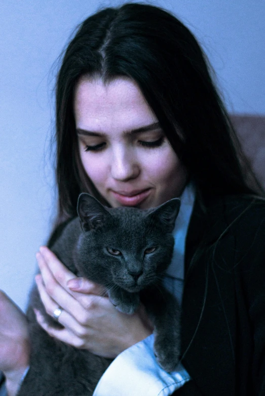 a woman holding a gray cat while looking at it