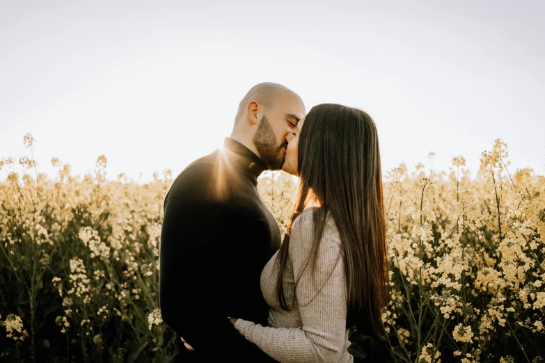 a man kissing his woman while in a field of flowers