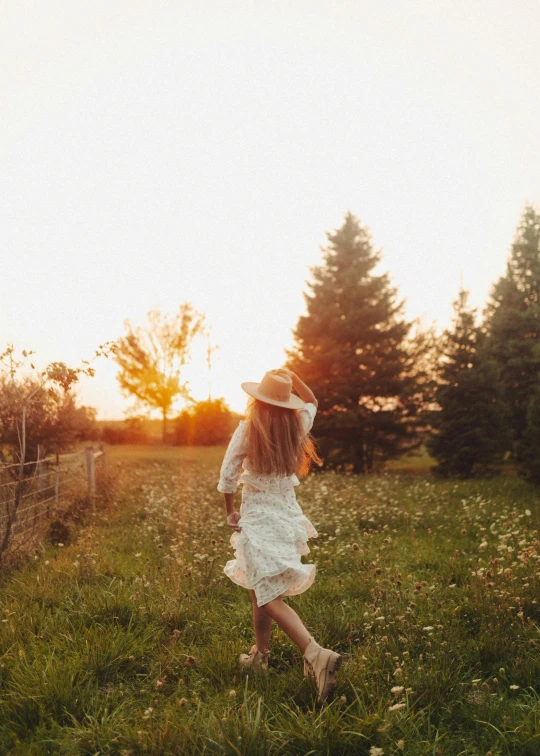 girl in a white dress and hat walking in a field