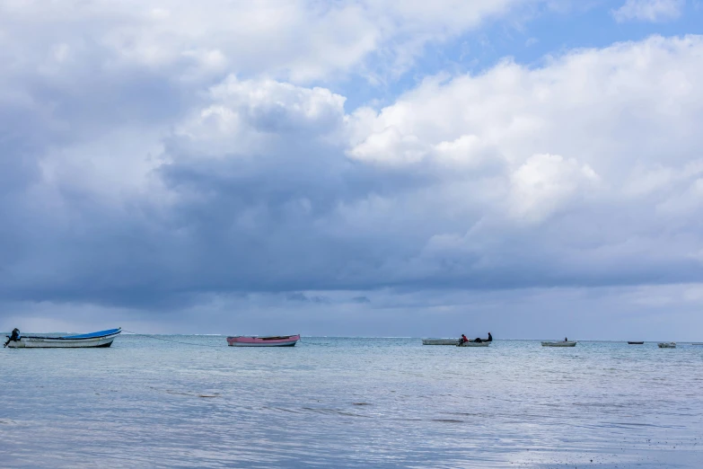 several boats floating on the ocean under cloudy skies