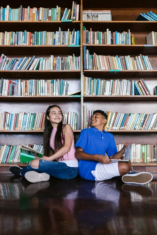 two children sit on the floor with books and headphones