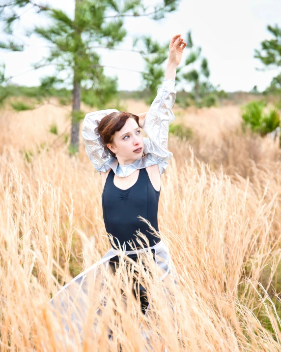 woman in dress in field of tall brown grass with trees in the background