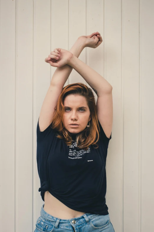 a woman posing with her arms up, while standing in front of a wall