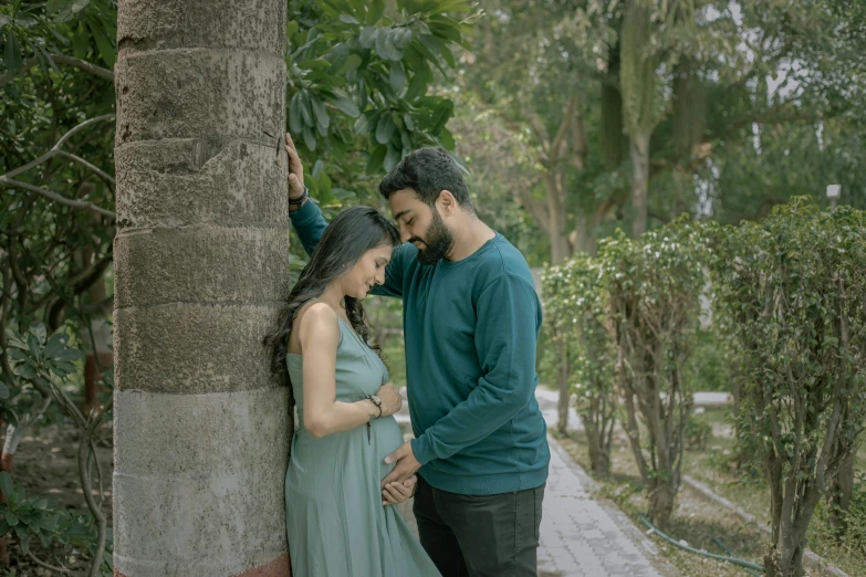 a pregnant couple are cuddling around a tree