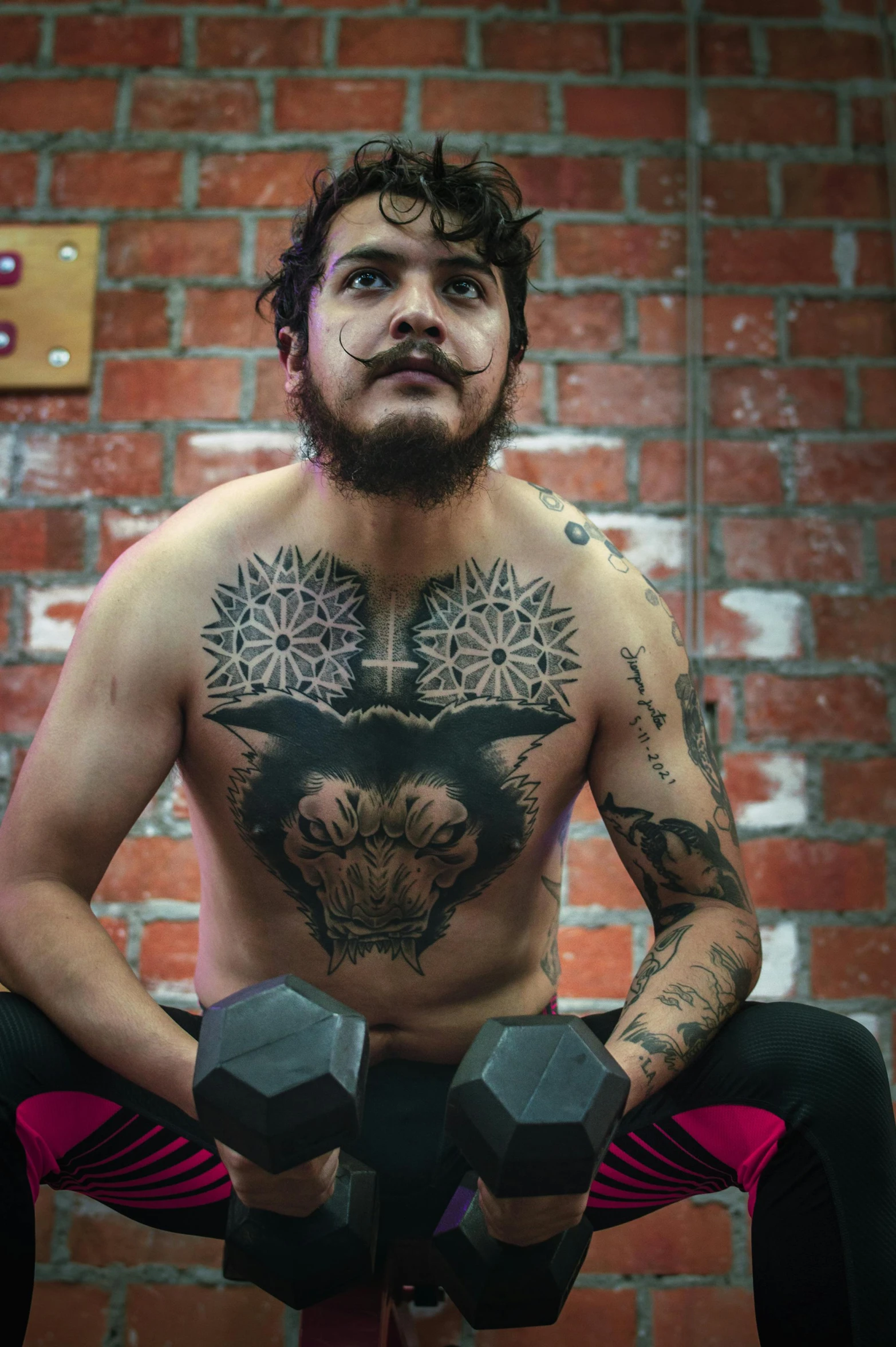 a man holding two dumbbells sitting in front of a brick wall