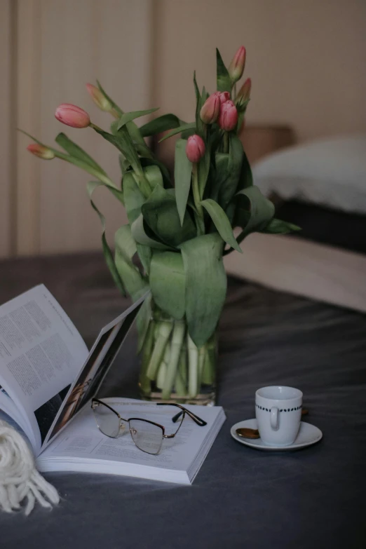 a vase with pink flowers, a cup of coffee and a book