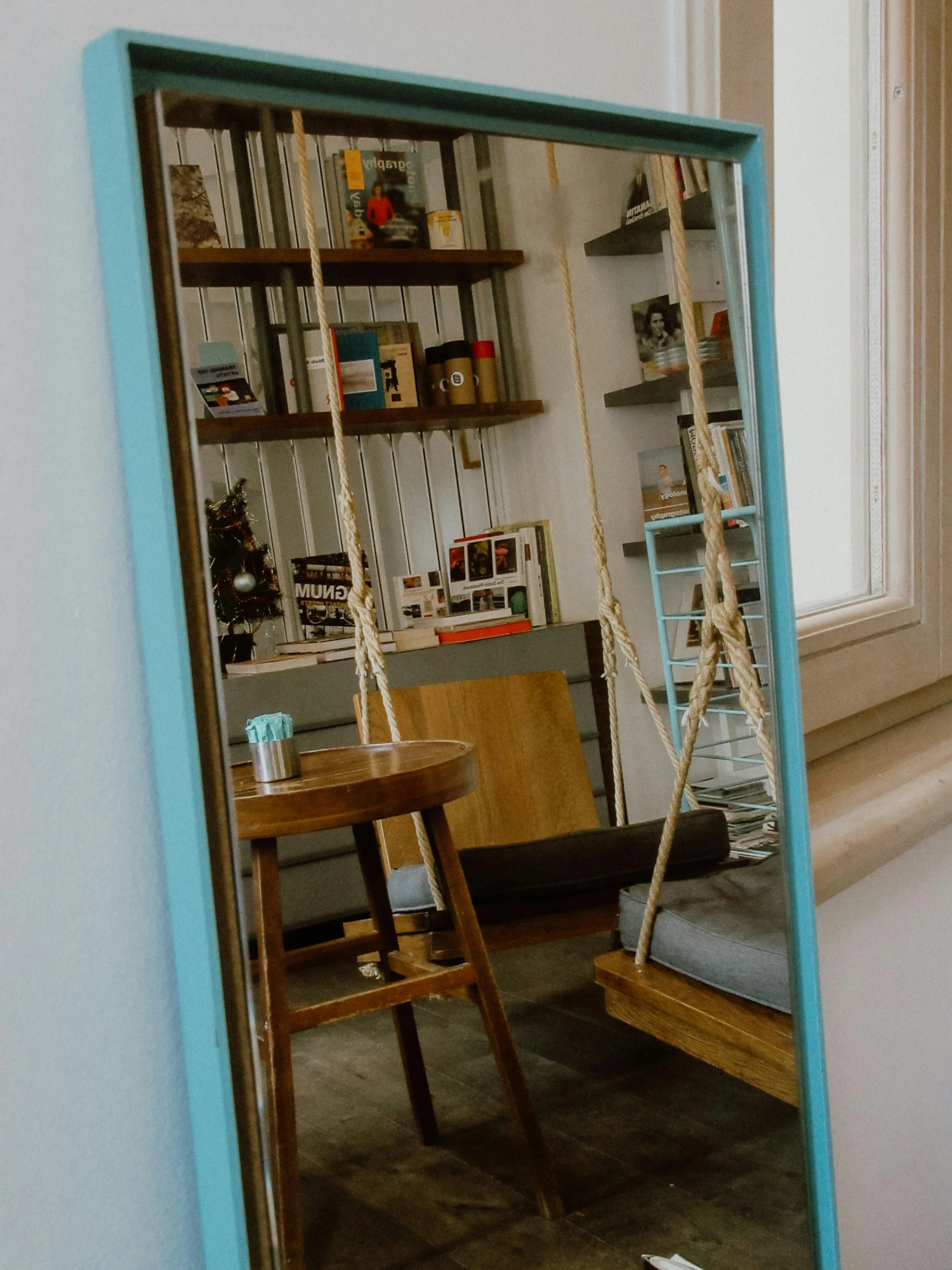 a mirror reflection shows a chair, ladder and shelves in a room