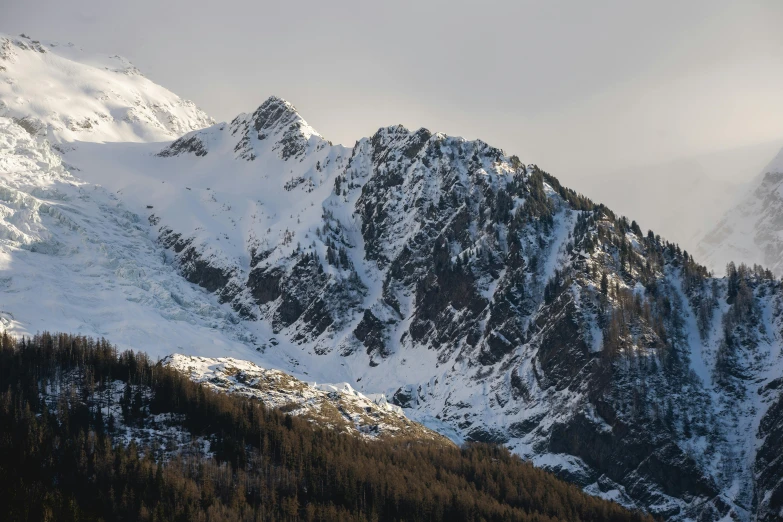 snow - capped mountains rising above forest with clouds