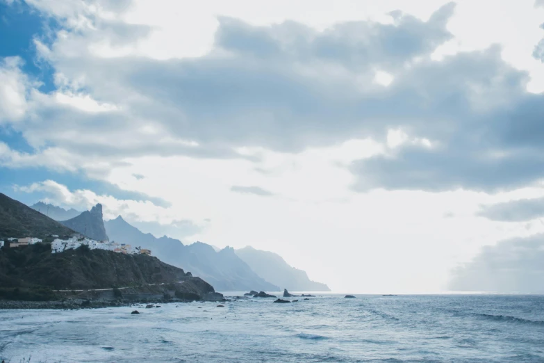 a picture of the ocean with houses on the cliff in the distance