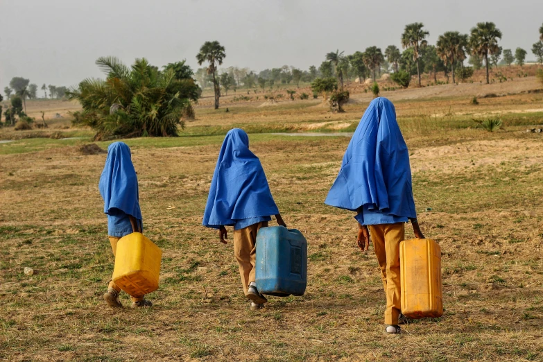 the people walk through an open field with their luggage in blue capes