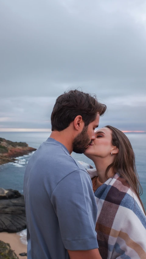 a man and woman kissing and standing near the ocean