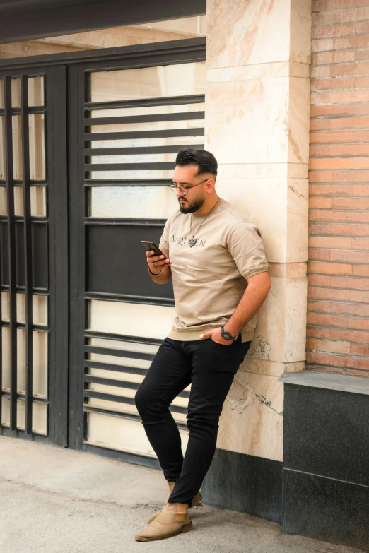 a man leaning against a wall, looking at a cellphone