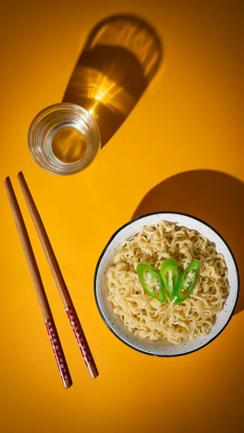 a plate of noodles and chopsticks with a tea kettle on the side