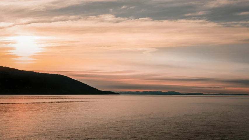 a hill is seen across the water at sunset