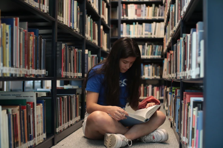 a young woman is sitting on the floor in a liry reading a book