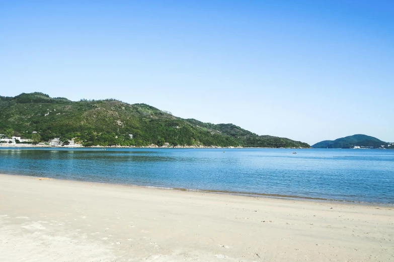 a beach with blue ocean water and a hill in the background