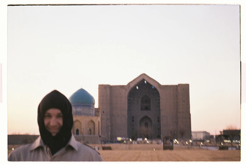 a man in a hooded jacket standing outside of a mosque