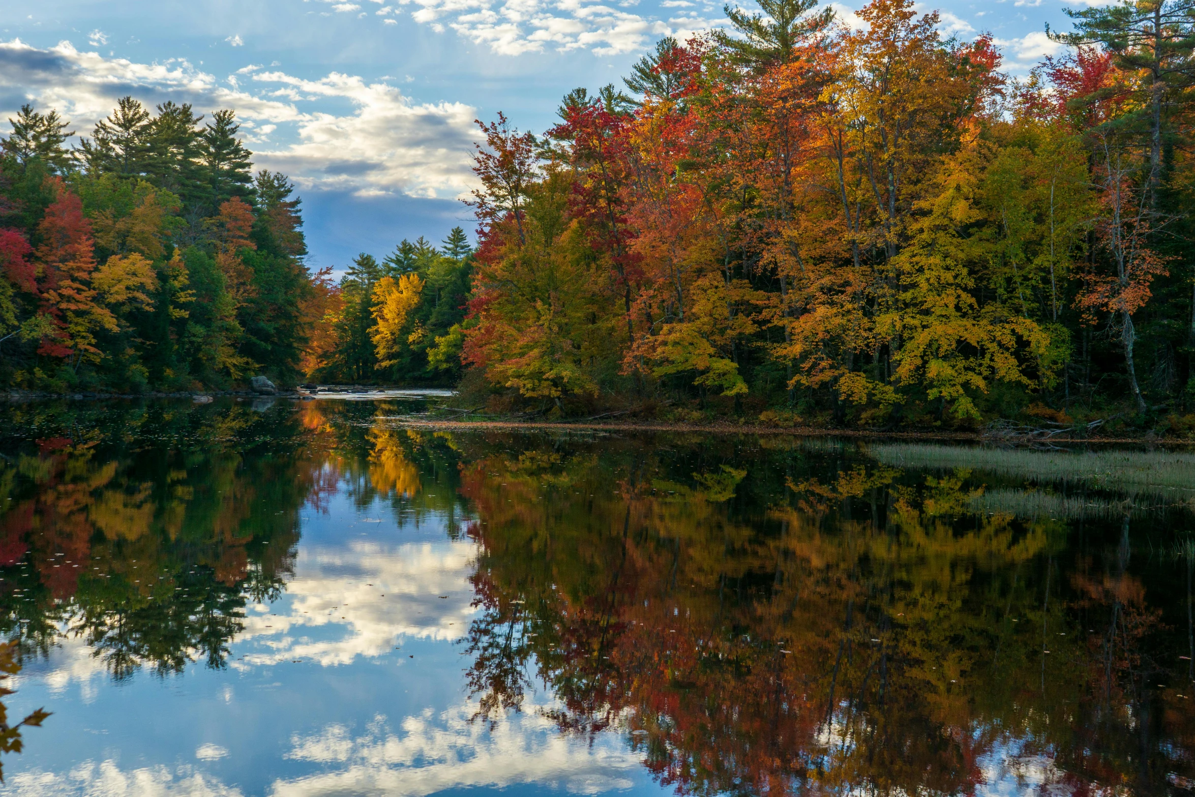 a lake surrounded by autumn colored trees with clouds