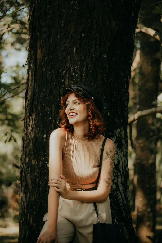 a woman standing next to a tree while wearing a hat