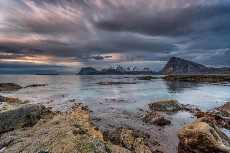 the cloudy sky over a rocky beach and mountain