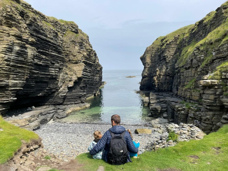 a man and child are sitting on rocks near the ocean