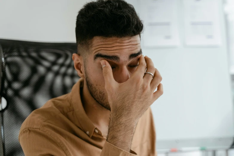 a man in a brown shirt holds his head while holding his hands to his temples