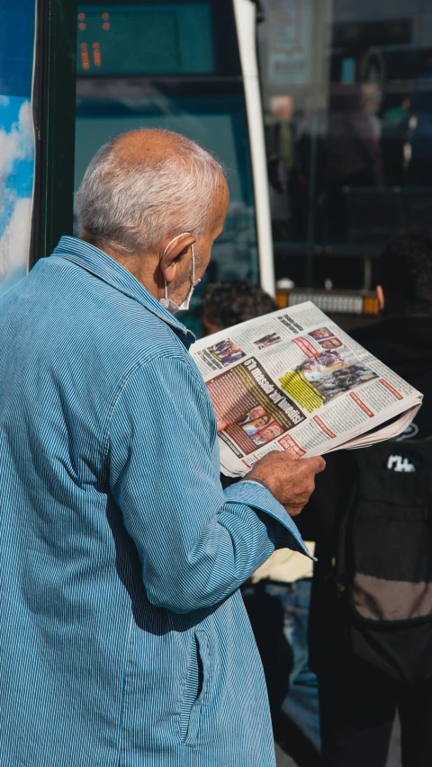 old man standing outside looking at newspaper while reading it