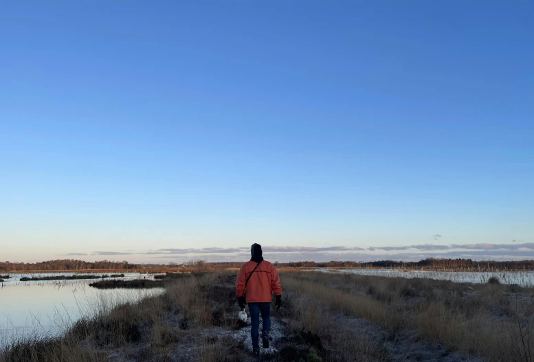 the woman is walking alone through a field next to the water