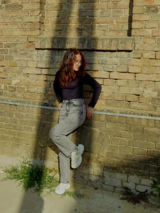 a woman is leaning against a brick wall posing for a po