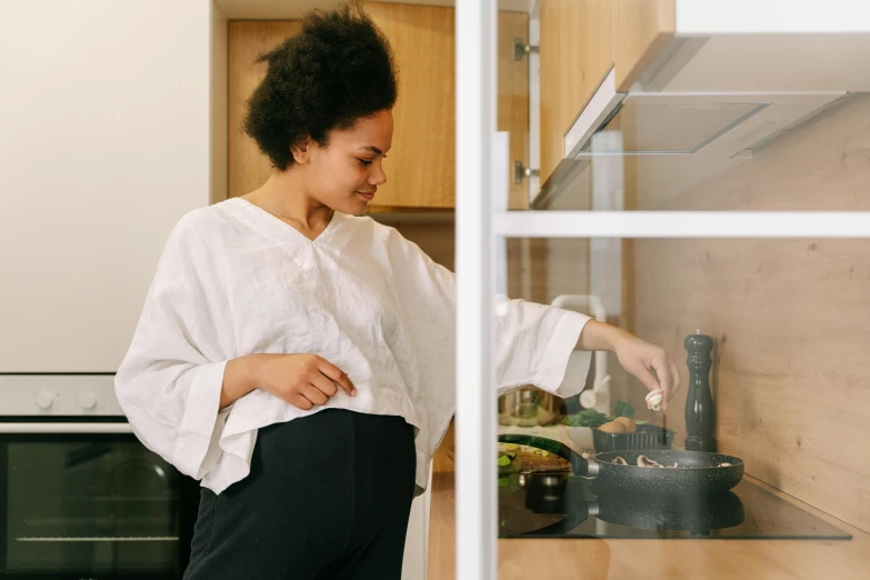 a woman is putting soing in the pot while looking through the glass door