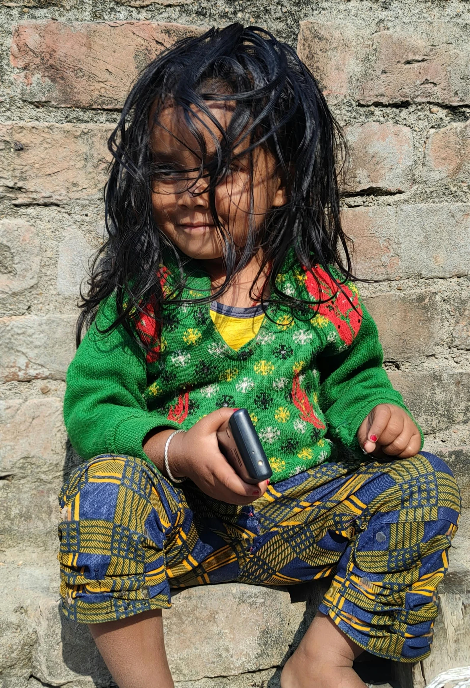 a  sitting on a brick wall holding a cell phone