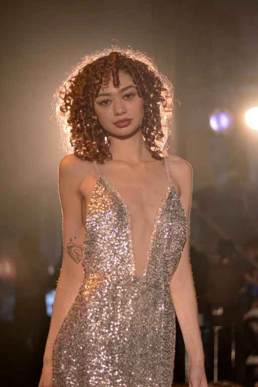 a woman in a silver gown standing on a runway