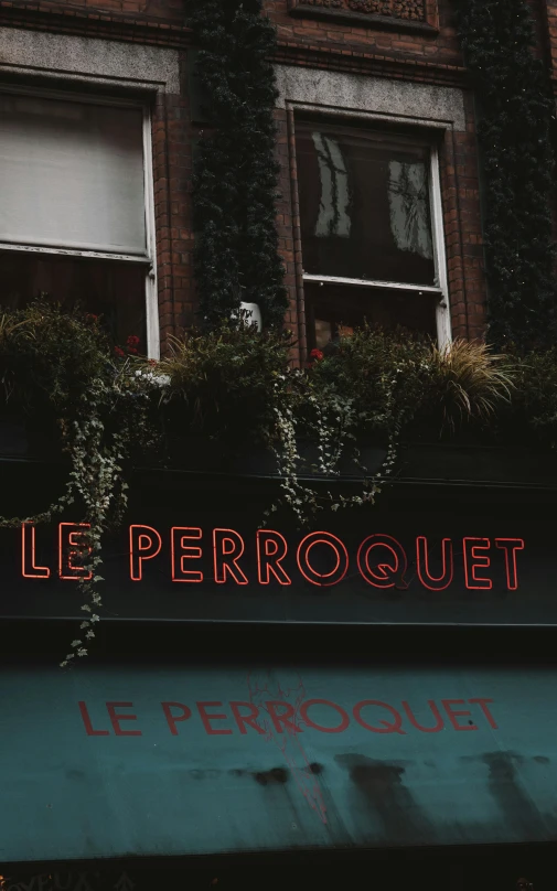 a restaurant sign for le perroquit and with a lot of green bushes growing on the front