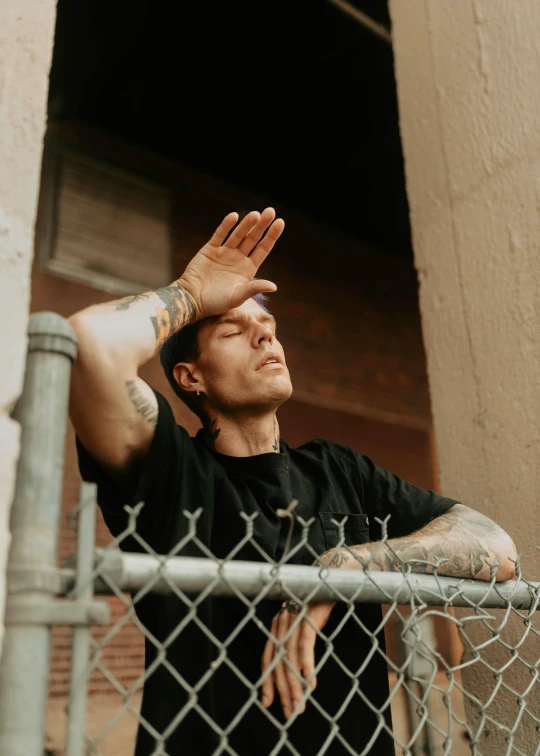 a man wearing tattoos next to a fence with his arms above the top