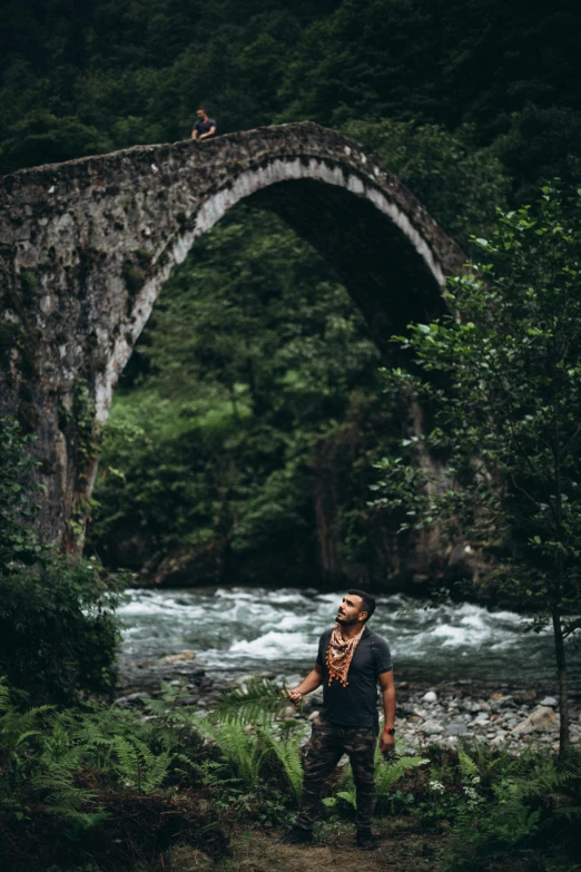 a man standing next to a stone bridge