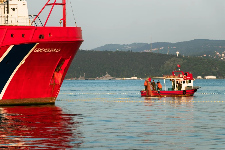 a boat that is on the water in front of a large red and white ship