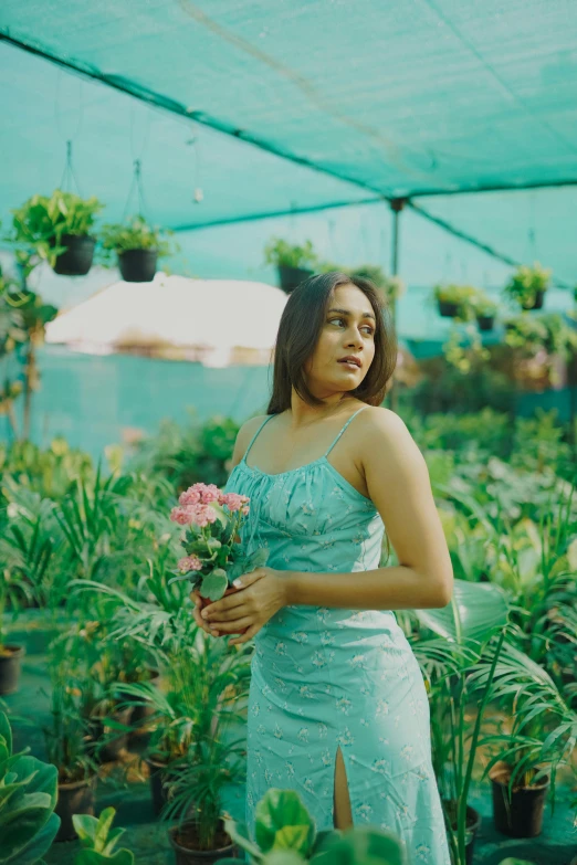 a woman in a blue dress stands by potted plants