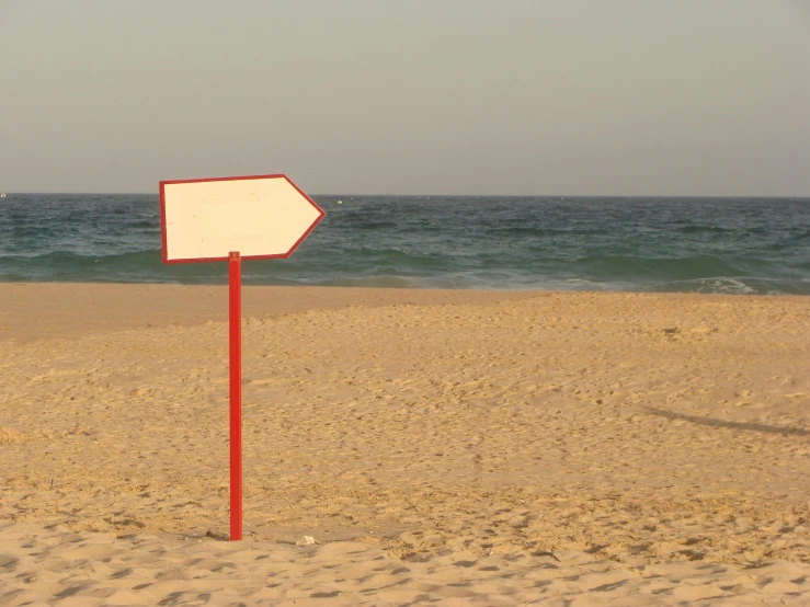 a sign on a beach near water with sky in the background