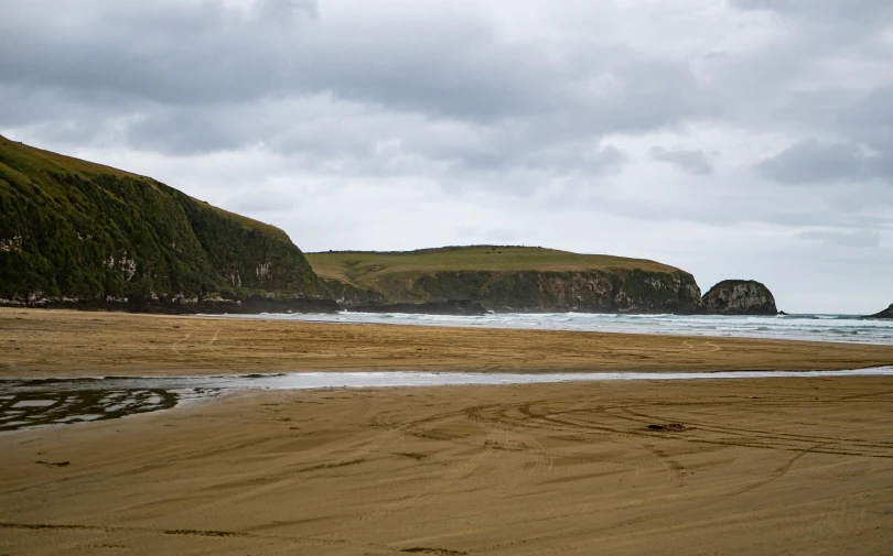 a very cloudy day at the beach with the ocean and a mountain in the distance