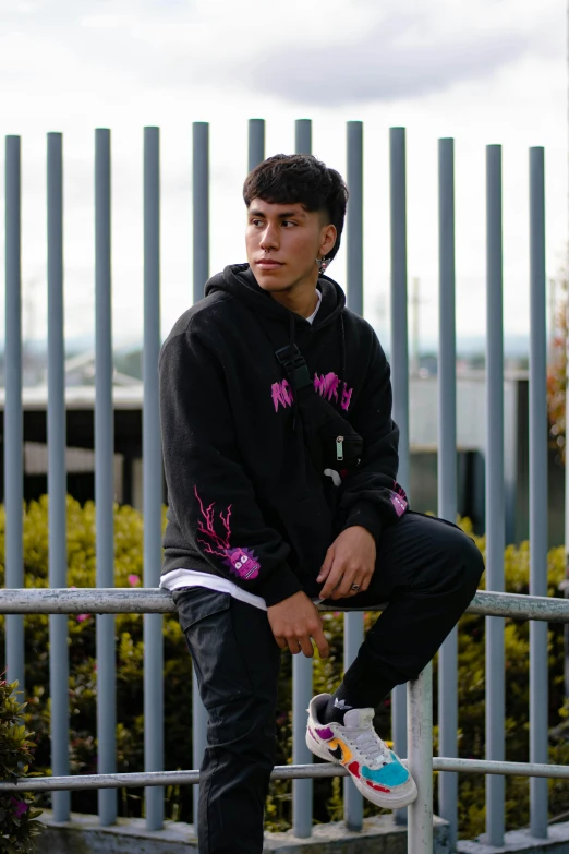 a young man in a black hoodie is standing on the fence